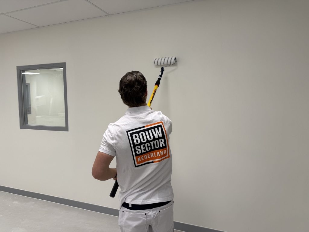 Schilder rolt een witte wand in een lege ruimte met een binnenraam