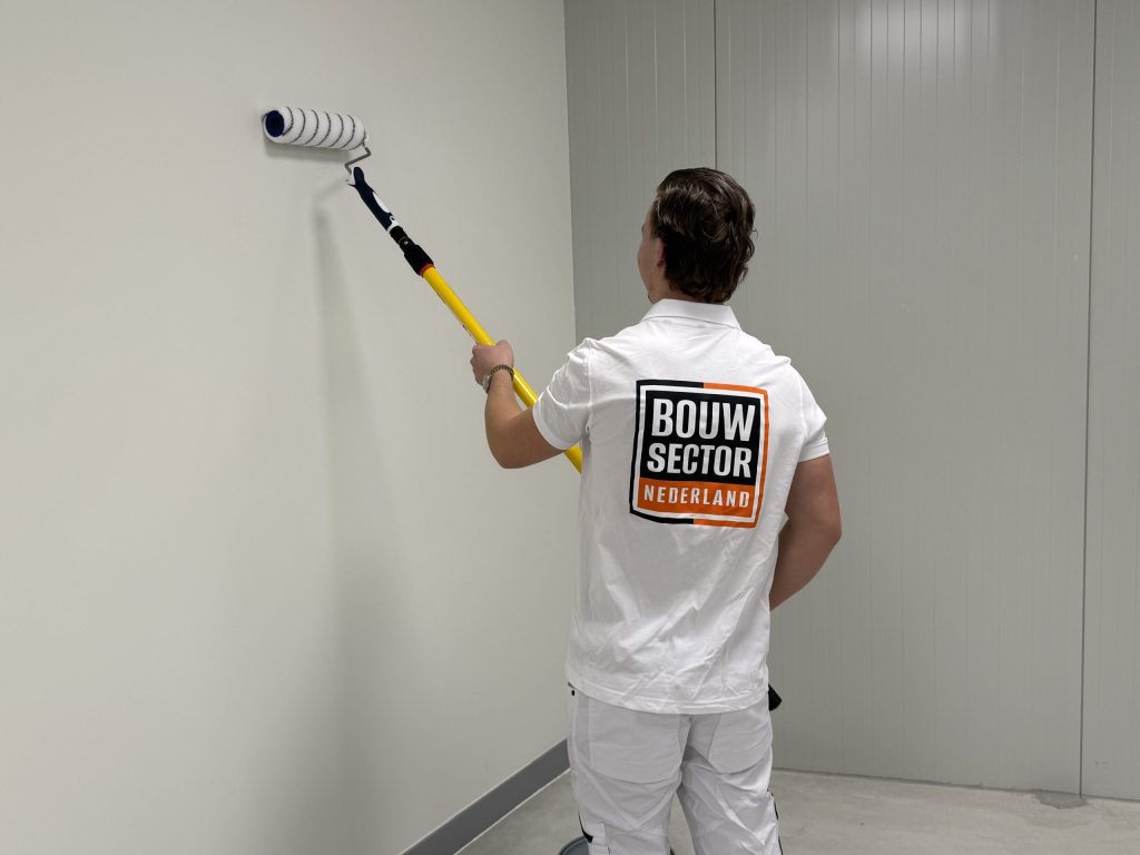Schilder van Bouwsector Nederland zet een baan witte verf op een lege wand