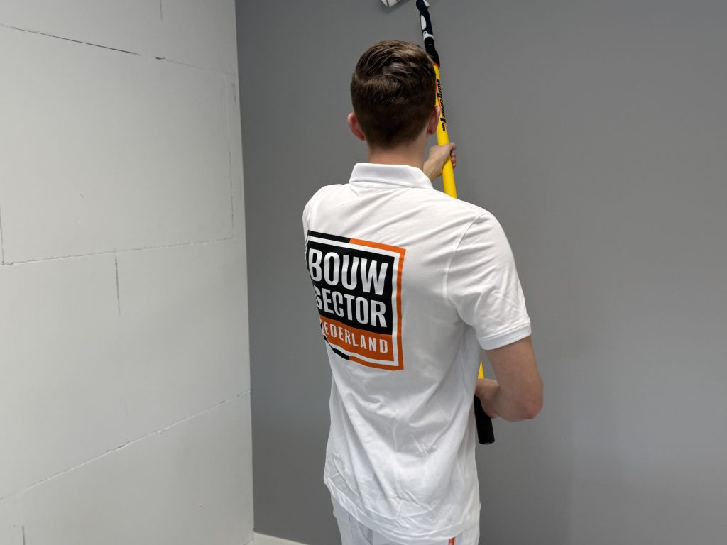 Schilder met logo van Bouwsector Nederland rolt een grijze muur met een lange roller