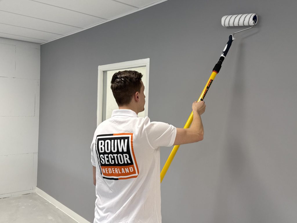 Schilder rolt een grijze wand vlak naast een deur met een wit gelakt kozijn