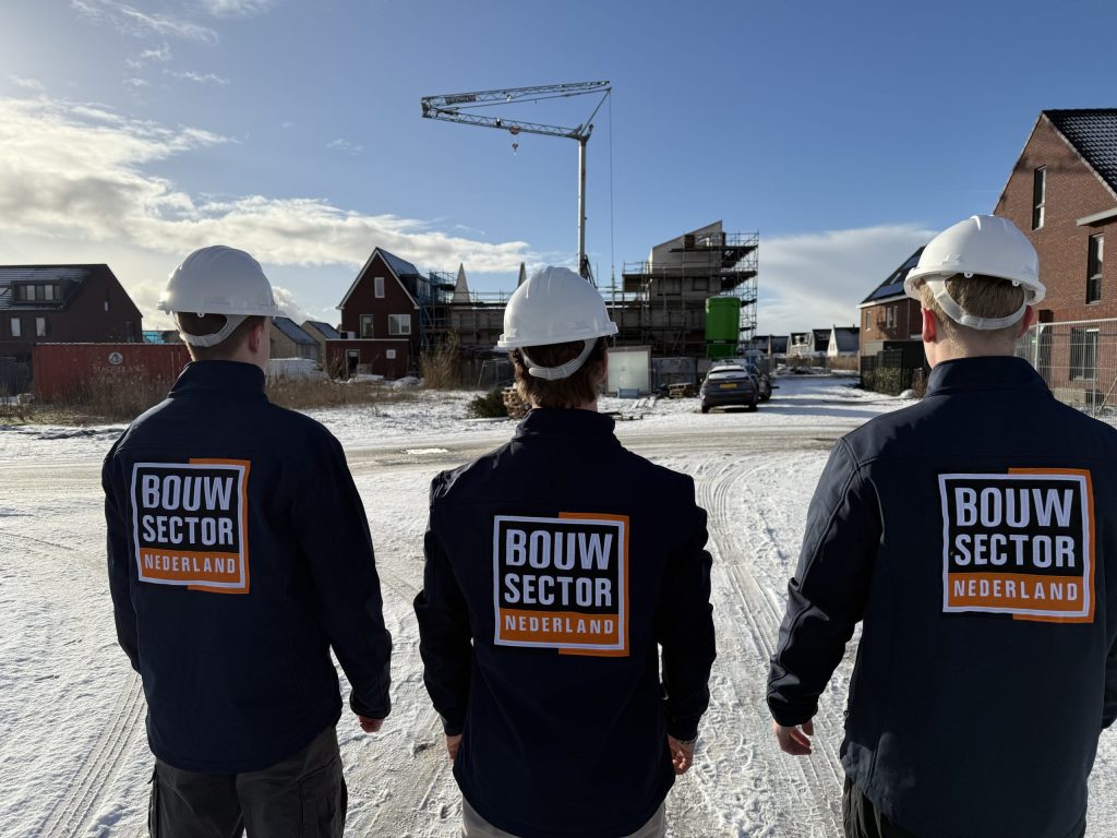 Drie mannen in jas van Bouwsector Nederland lopen door een straat met nieuwe bakstenen woningen