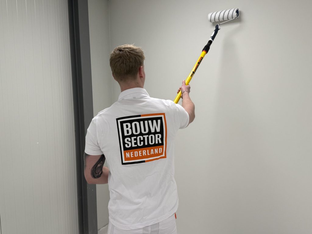 Schilder van Bouwsector Nederland rolt een lichte wand naast een wand van verticale panelen