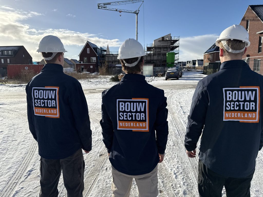 Drie vakmensen van Bouwsector Nederland met witte helm op een nieuwbouwlocatie in de sneeuw